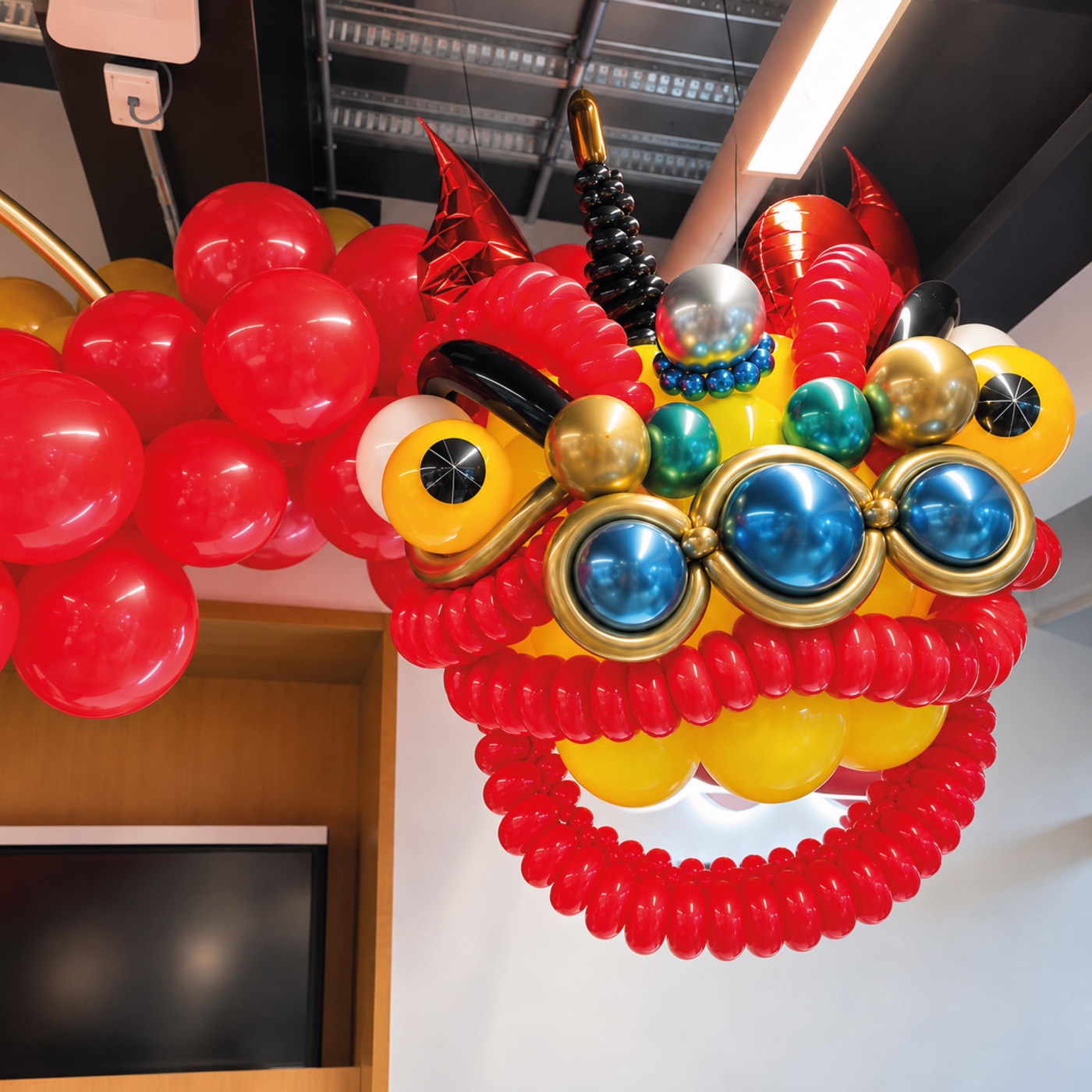 Dragón de globos rojos, amarillos y metálicos suspendido en un interior